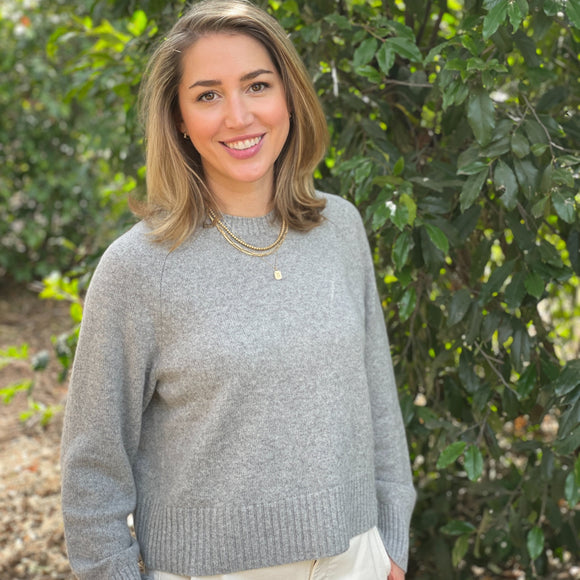 Woman wearing a gray sweater standing in front of green foliage