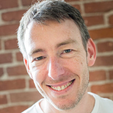 Man with gray hair and a beard smiling in front of a brick wall