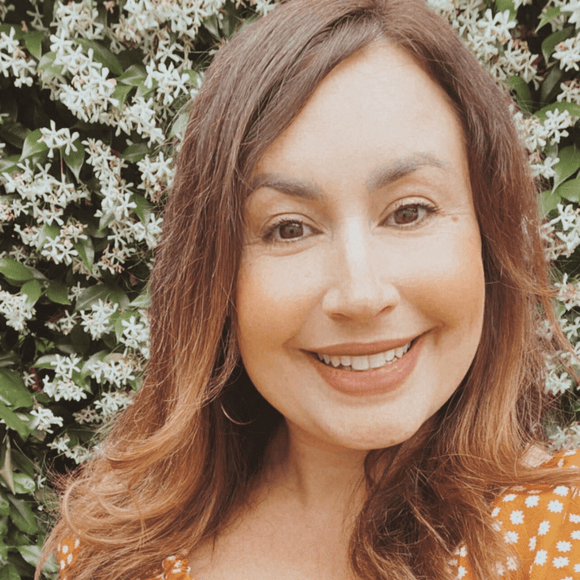 Woman with long brown hair smiling in front of a floral background